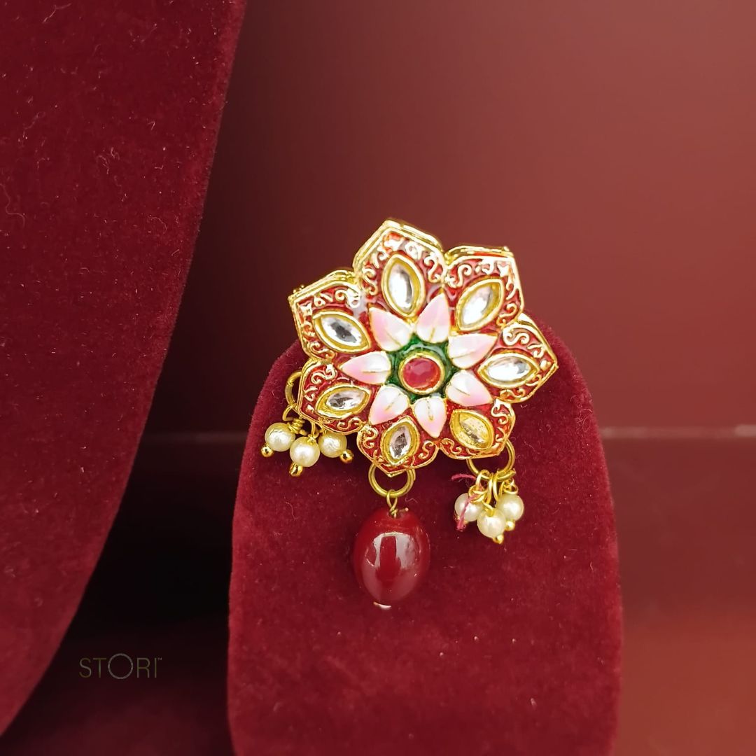 Decorative gold ring with gemstones and a red bead on a red velvet stand.