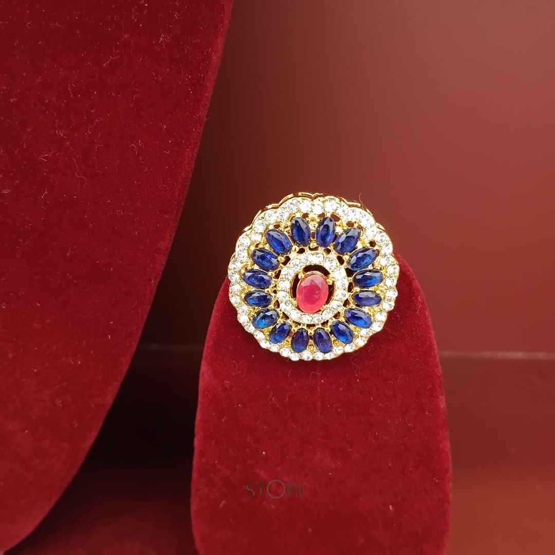 Decorative ring with blue stones and a red gemstone on a red stand against a brown background