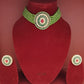Green beaded necklace with red gemstone on a red velvet stand, accompanied by matching earrings.