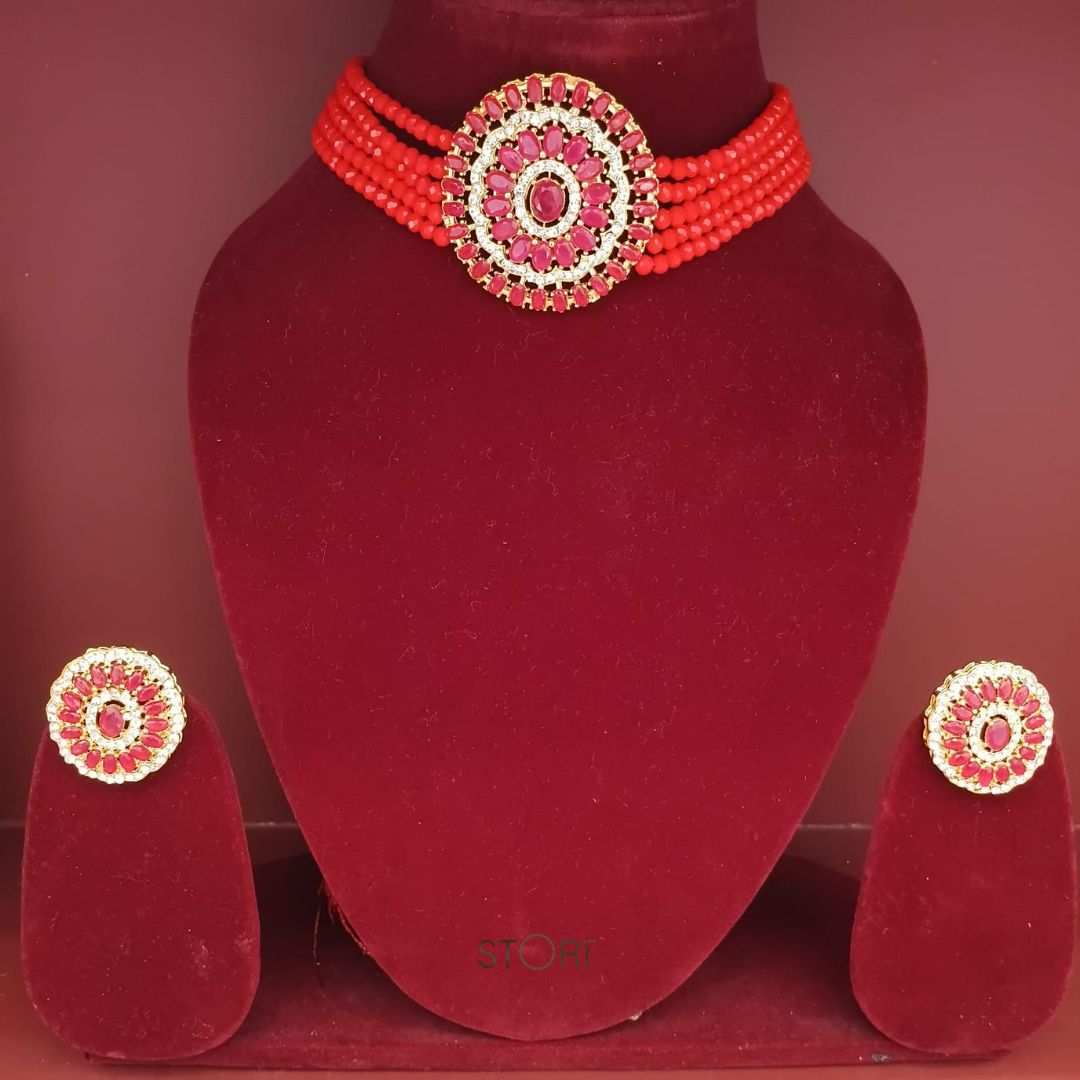 Red beaded necklace and earrings set on a red velvet stand.