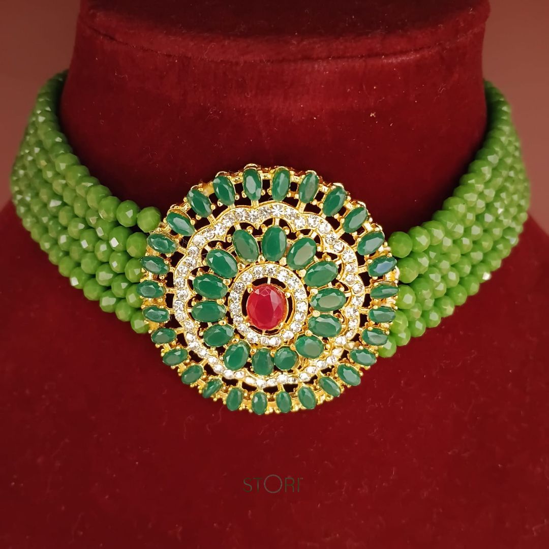 Green beaded necklace with a gold and red central pendant on a red background