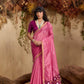 Woman in a pink saree with a floral border against a natural background