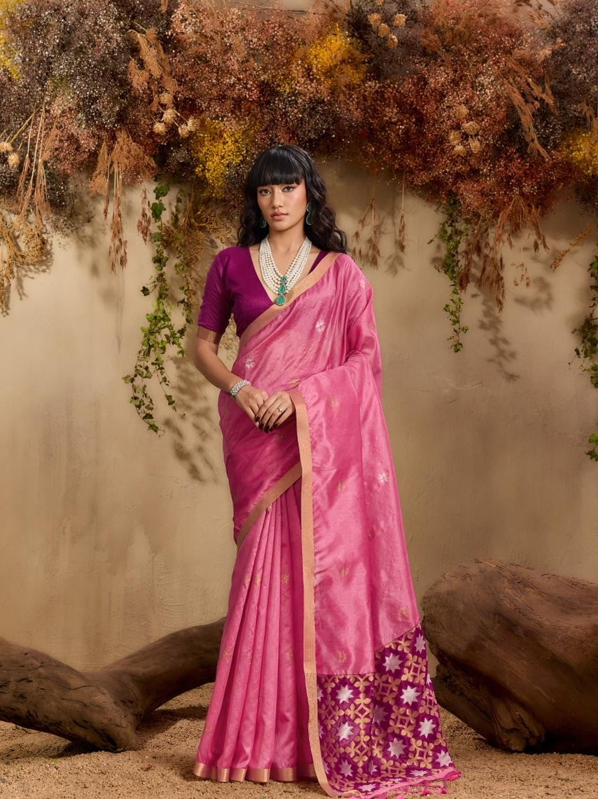 Woman in a pink saree with a floral border against a natural background