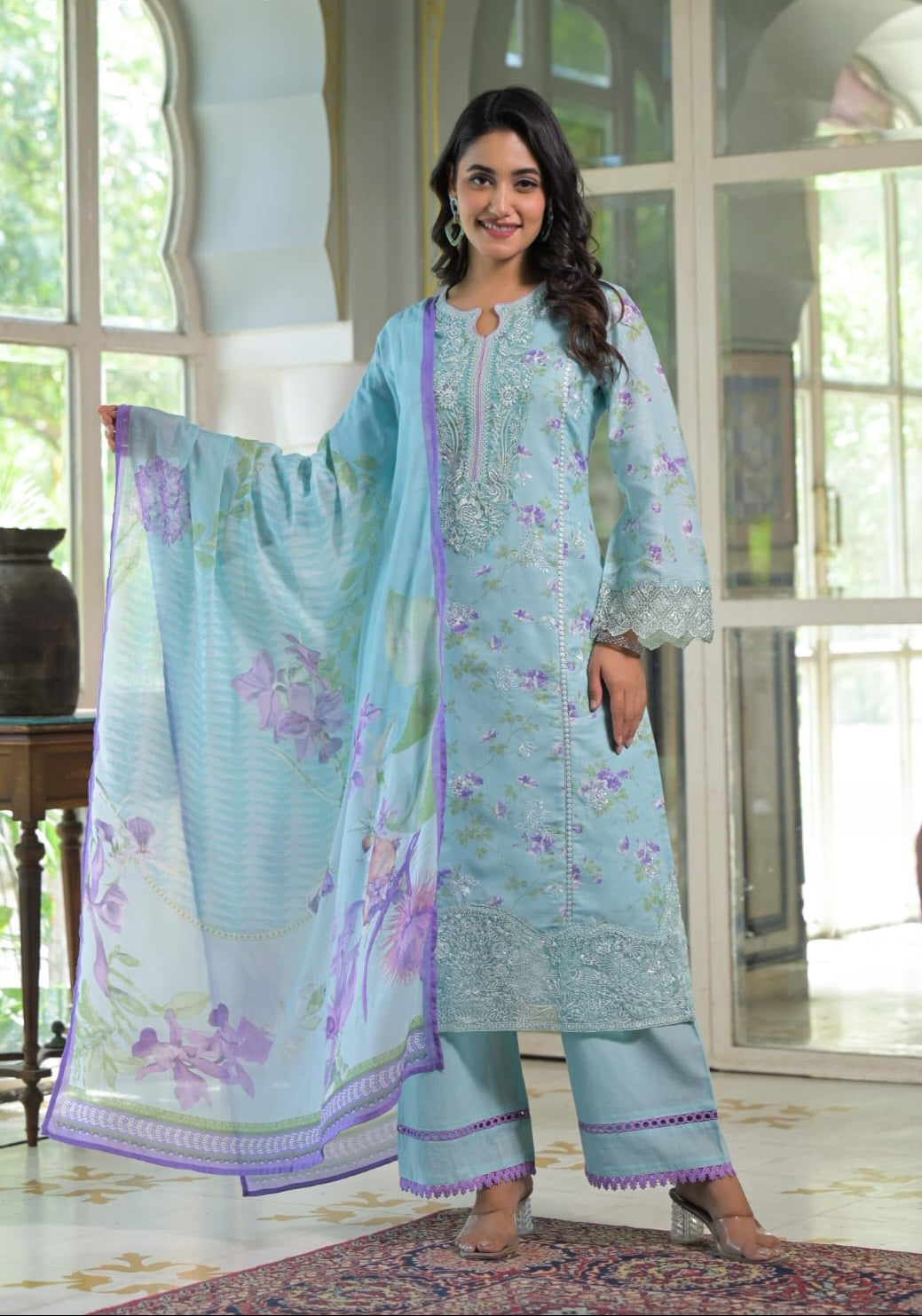 Woman wearing a light blue embroidered outfit with a matching dupatta in a bright room.